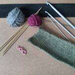 Verschiedene Garne, Srick- und Häkelnadeln, sowie eine gestrickte Maschenprobe.