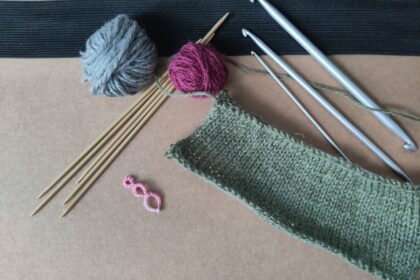 Verschiedene Garne, Srick- und Häkelnadeln, sowie eine gestrickte Maschenprobe.
