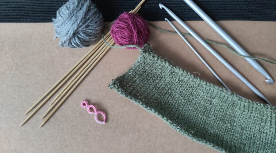 Verschiedene Garne, Srick- und Häkelnadeln, sowie eine gestrickte Maschenprobe.