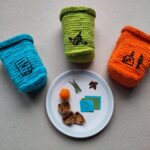 drei Gehäkelte Mülltonnen in blau, grün und orange sind um einen Teller mit Müllteilchen arrangiert.