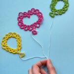 Drei Luftballons, die in Occhitechnik erstellt wurden vor blauem Hintegrund. Eine Hand hält alle drei Ballons an ihren Schnüren