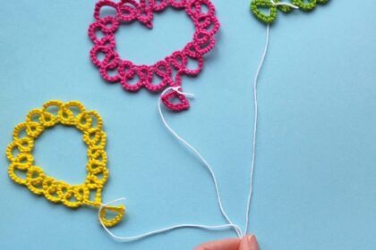 Drei Luftballons, die in Occhitechnik erstellt wurden vor blauem Hintegrund. Eine Hand hält alle drei Ballons an ihren Schnüren