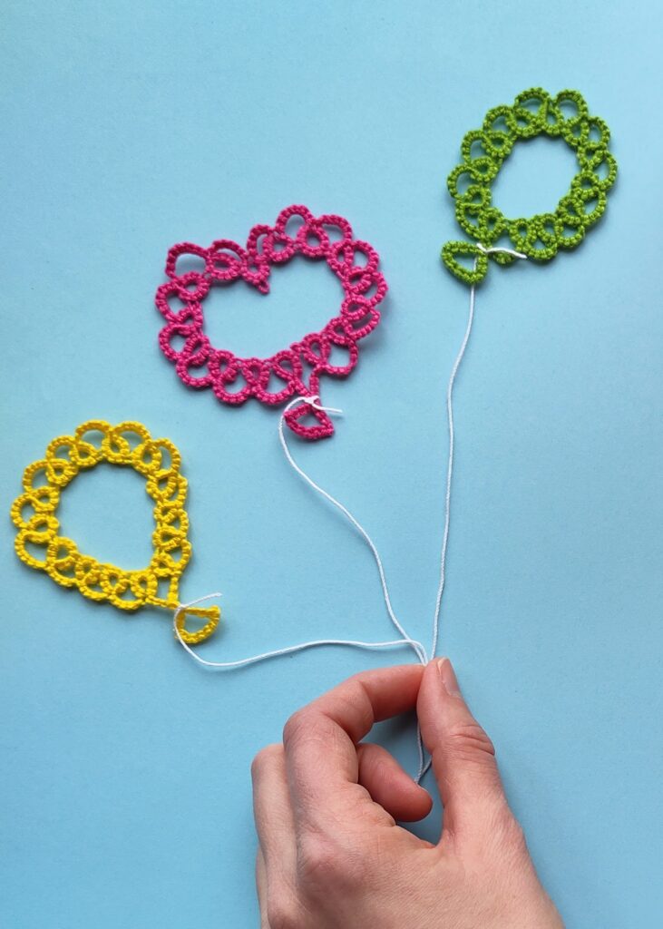 Drei Luftballons, die in Occhitechnik erstellt wurden vor blauem Hintegrund. Eine Hand hält alle drei Ballons an ihren Schnüren