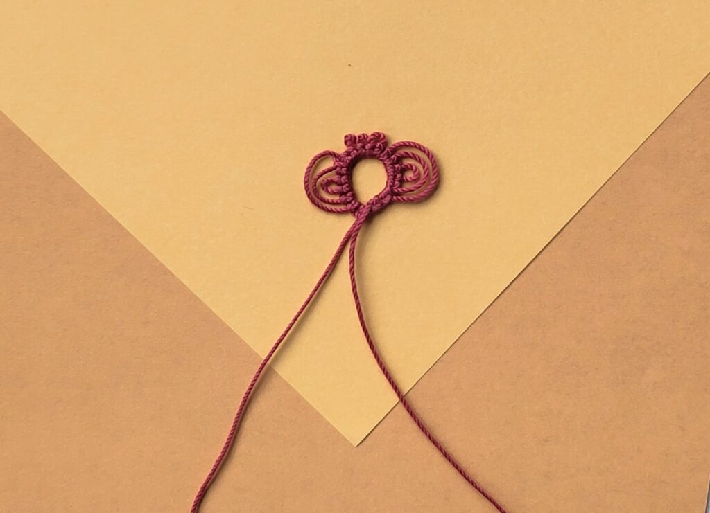 Ein roter Occhiring auf gelbem Grund mit zwei Tripelpicots und drei einfachen Picots