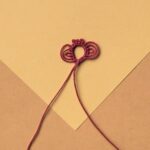 Ein roter Occhiring auf gelbem Grund mit zwei Tripelpicots und drei einfachen Picots