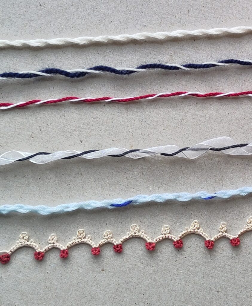 Fünf verschiedene handgedrehte Kordeln in maritimen Farben (Blau, Rot, Weiß) aus Wolle und Schleifenband. Eine weiß-rote Occhiborte, die ein wenig, wie eine Kordel aussieht.