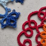 Ein blaues und ein rotes Stück Occhi-Spitze liegen sich gegenüber.