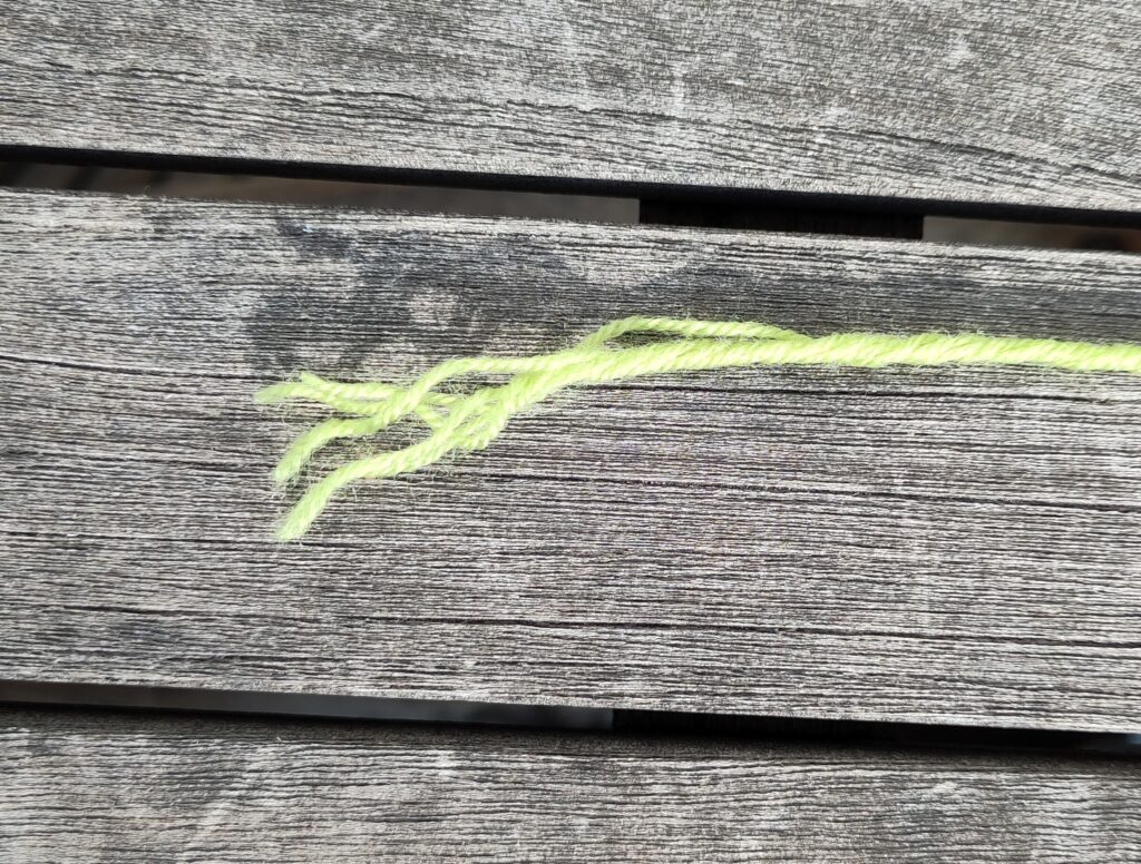 Ein ausgefranster grüner Wollfaden auf einem Holztisch in der Sonne