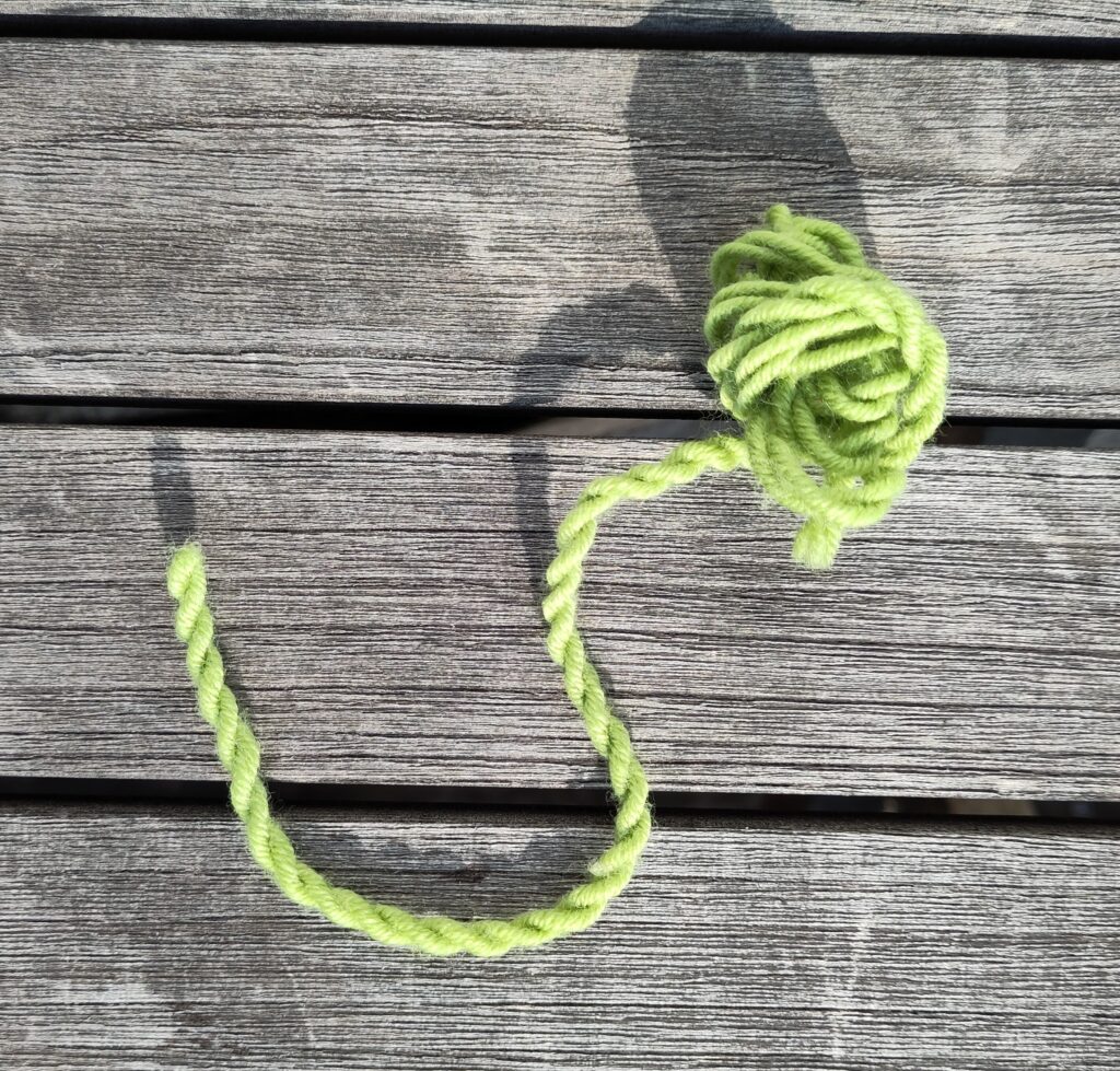 Eine zweifädige grüne Kordel aus Wolle auf einem Holztisch in der Sonne