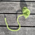 Eine zweifädige grüne Kordel aus Wolle auf einem Holztisch in der Sonne