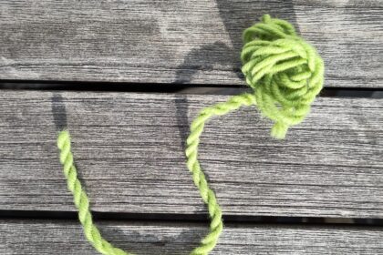 Eine zweifädige grüne Kordel aus Wolle auf einem Holztisch in der Sonne