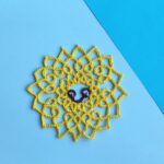 Eine lächelnde gelbe Sonne in Occhitechnik geknotet.