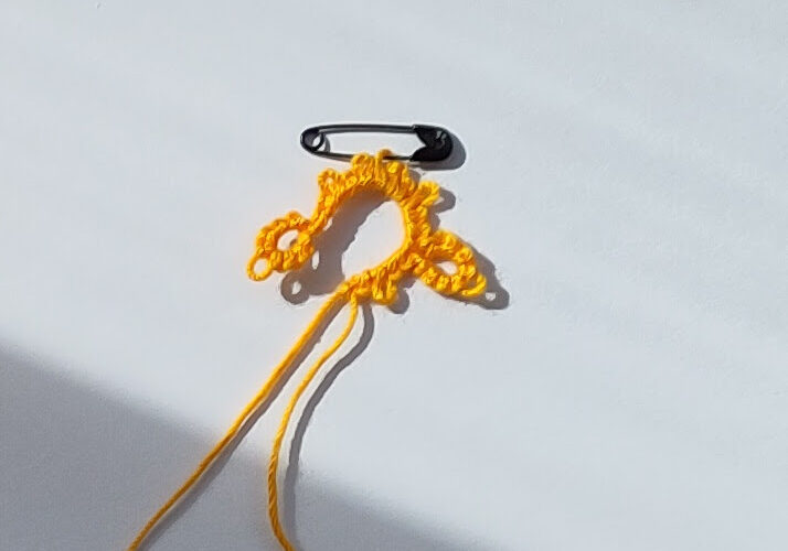 Eine Angefangene Occhiarebit mit einer Minisicherheitsnadel als Maschenmarkierer an einem Picot