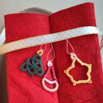 Drei Weihnachtsanhänger in Occhitechnik an hellem GEschenkband an rotem Filz.