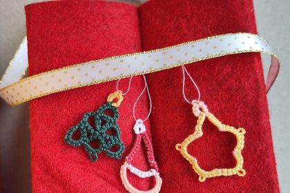 Drei Weihnachtsanhänger in Occhitechnik an hellem GEschenkband an rotem Filz.