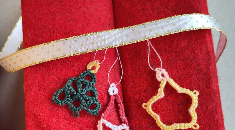 Drei Weihnachtsanhänger in Occhitechnik an hellem GEschenkband an rotem Filz.