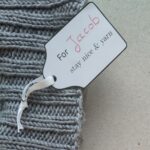 Ein Geschenkanhänger mit handschriftlich ergänztem Namen an einem Strickstück