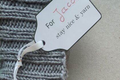 Ein Geschenkanhänger mit handschriftlich ergänztem Namen an einem Strickstück