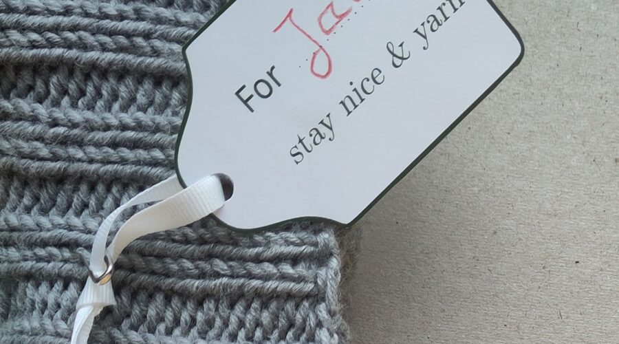 Ein Geschenkanhänger mit handschriftlich ergänztem Namen an einem Strickstück