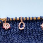 Ein Strickstück auf Bambusnadeln mit drei rosa Maschenmarkierern mit Perlen