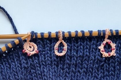 Ein Strickstück auf Bambusnadeln mit drei rosa Maschenmarkierern mit Perlen