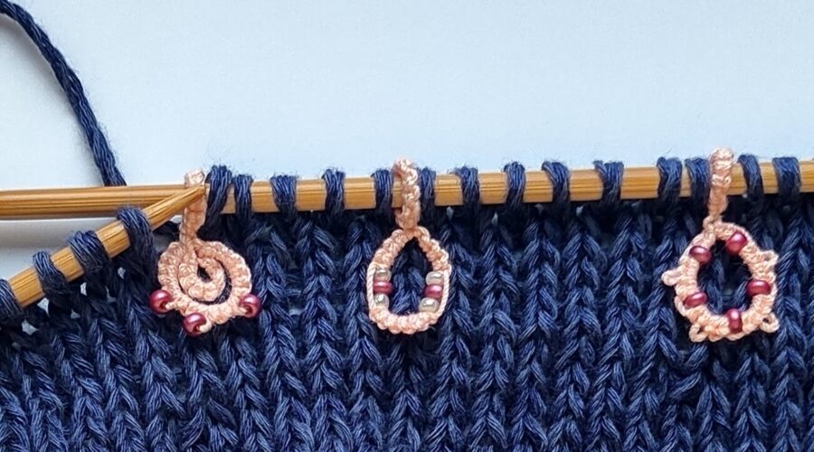 Ein Strickstück auf Bambusnadeln mit drei rosa Maschenmarkierern mit Perlen
